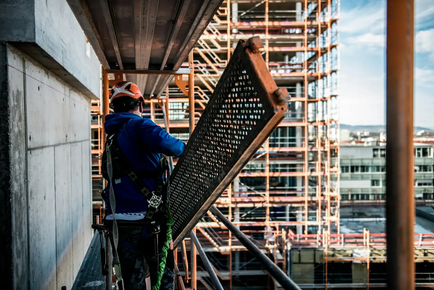 A scaffolder in a harness carrying a steel board along a scaffold