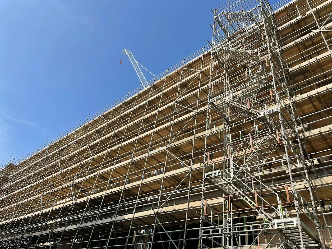 A long commercial building wrapped in scaffolding, with a crane behind