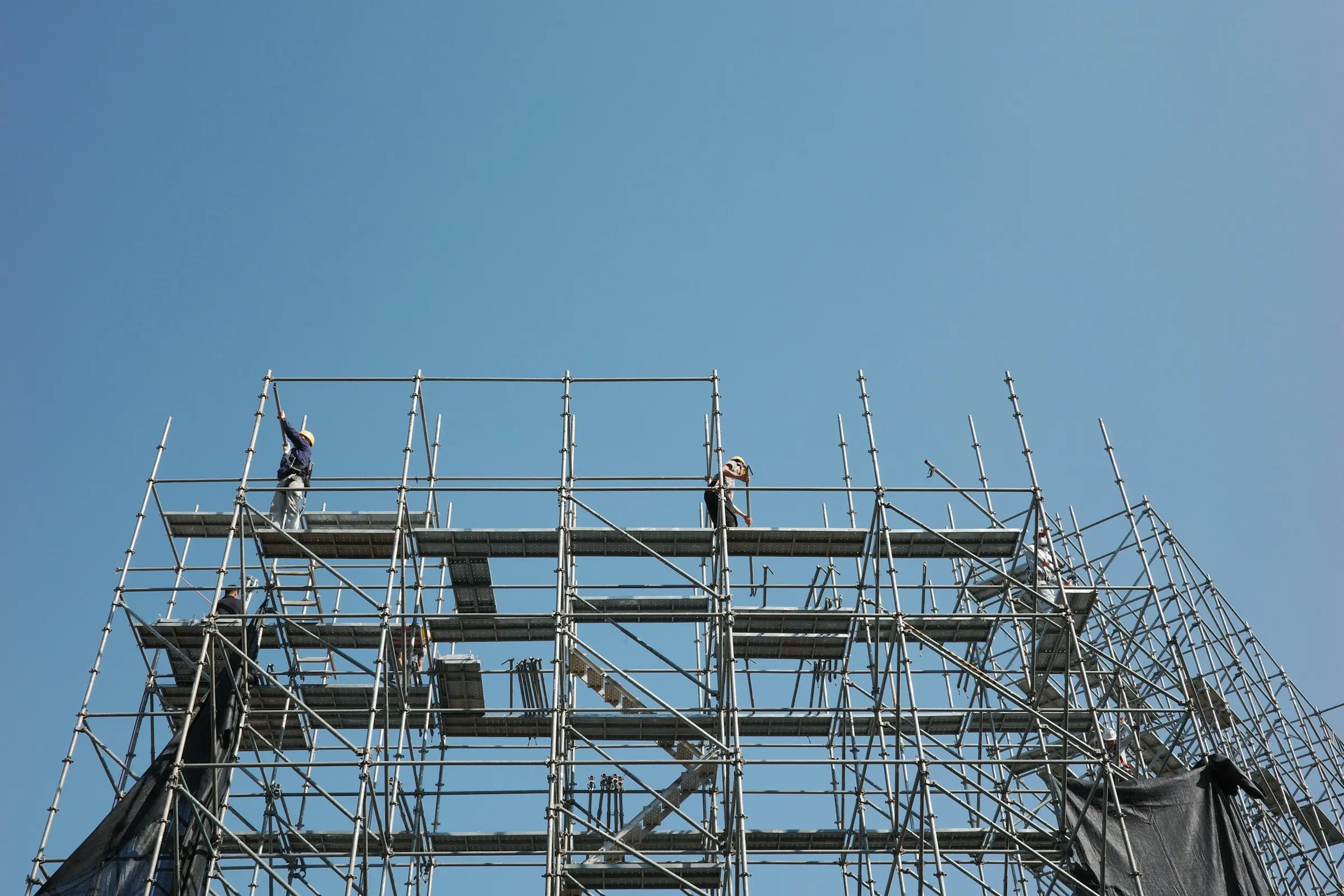Scaffolders working on the top lift of a tall scaffold against a clear blue sky