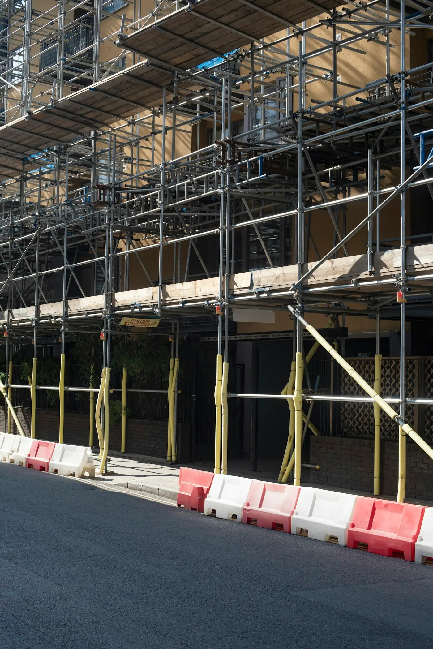 A scaffold along the front of a building, with barriers on the road beside it