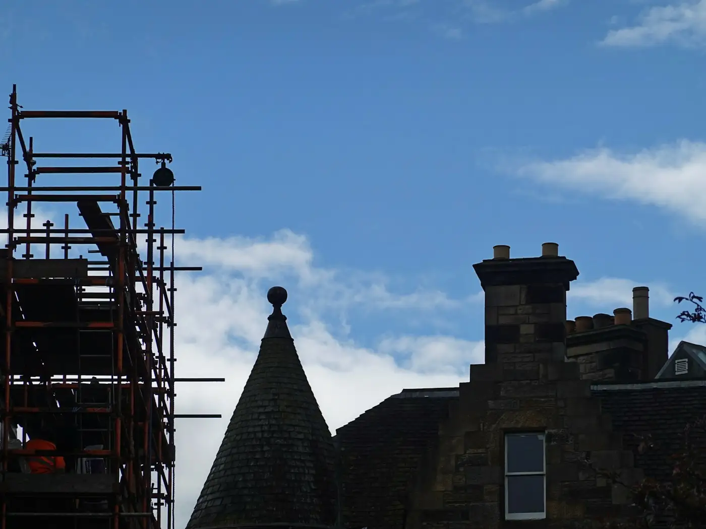 Scaffolding up to the chimneys of a stone house with a turret